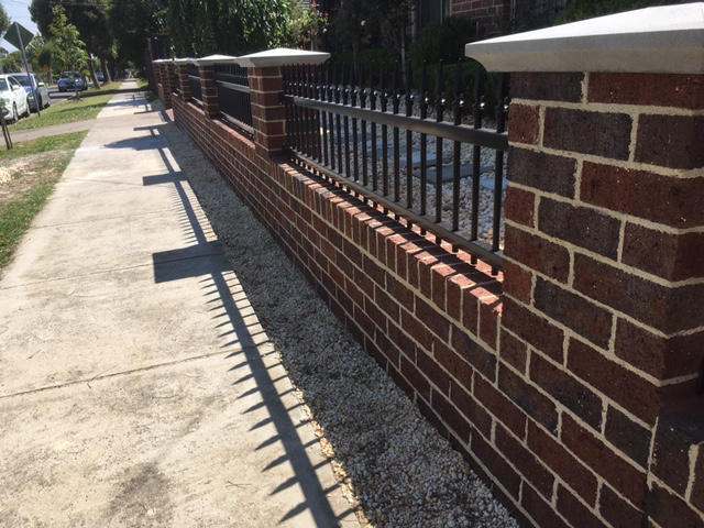 Red brick boundary wall with iron panels along a footpath